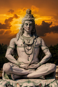 Majestic statue of Hindu Lord Shiva in serene meditating yoga pose against dramatic golden sunset sky with clouds in Rishikesh, Uttarakhand, India, spiritual concept, closeup