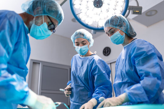Surgeon and female doctors performing surgery in hospital operating room. Medical team wearing scrubs and surgical masks during successful operation under bright surgical lights.