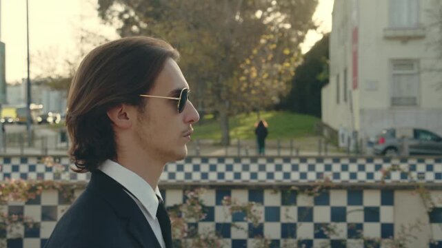 Young stylish man  in business suit is walking on the street. Young Confident businessman walks in the city in a gold sunglasses. Stylish White man with brown hair is walking in the city on the summer