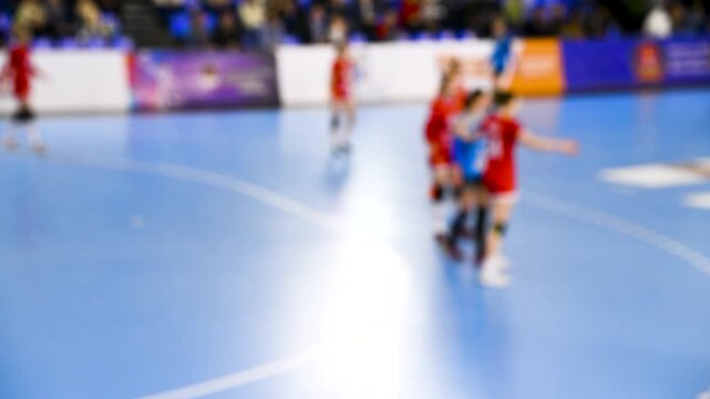A women's sports team plays indoor handball. Blurry.