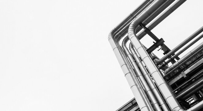 Abstract industrial metal pipes form repeating geometric patterns against a bright sky