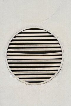 Front view of a circular louvered ventilation grill built into a light concrete facade wall.