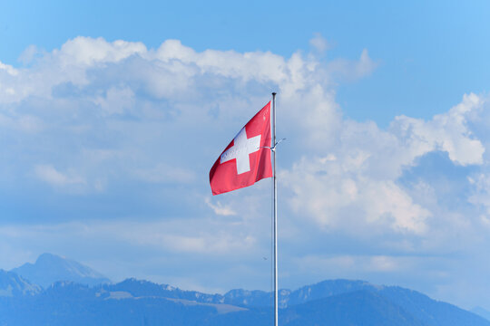 Swiss Flag Waving Proudly Against Blue Sky and Mountains in Morges
