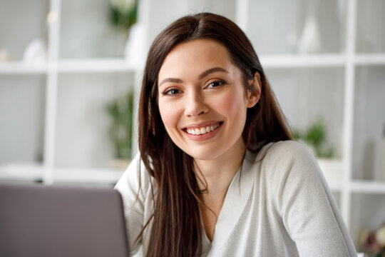 Portrait of a brunette woman working in an office with a laptop computer. A woman with a laptop looks into the camera and smiles sweetly.