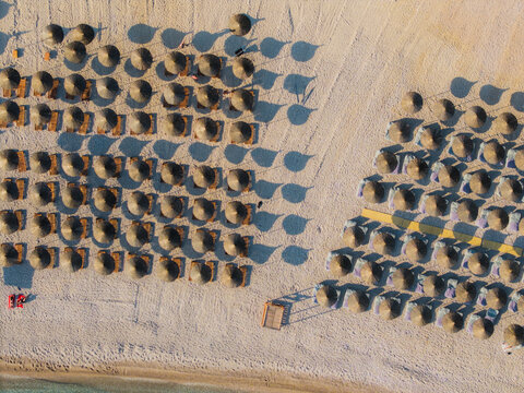 Aerial view of Llamani Beach featuring rows of straw umbrellas and sun loungers on the sandy shore in Himare, Vlore County, Albania.