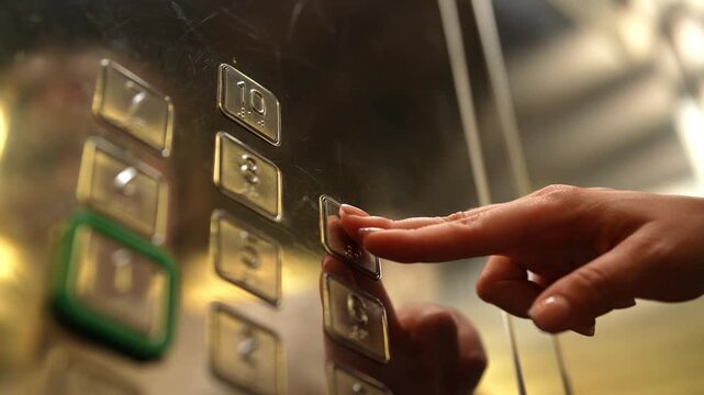 Close-up of female hand pressing ninth floor button on elevator panel. Finger pushing illuminated digit to select destination. Modern lift interior with shiny metal surface, close-up, slow motion.