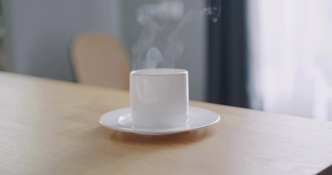 White porcelain tea cup sitting on wooden table with rising steam in quiet morning home.
