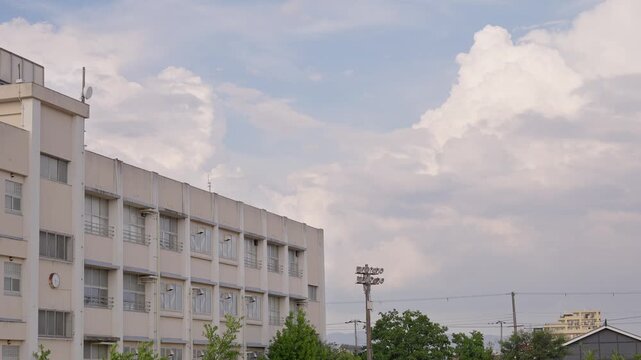 柔らかい光に包まれる夕暮れ時の校舎と背後で湧き上がる大きな入道雲