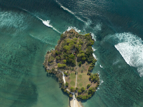 Aerial view of Nusa Dua Beach featuring a lush green peninsula surrounded by turquoise ocean waters and breaking waves in South Kuta, Bali, Indonesia.