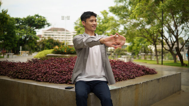 Young Asian remote worker stretching during a break from laptop work.