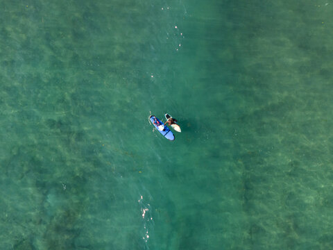 Aerial view of surfing training at Nusa Dua Beach with two surfers on boards in clear turquoise water in South Kuta, Bali, Indonesia.