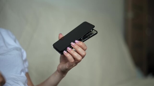 Cropped shot of person holding mobile device with damaged, swollen battery and detached screen, attempting to connecting charging cable to port. Concept of electronic waste and repair issues.