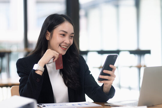 Asian businesswoman using a smartphone and holding a credit card for online shopping or mobile banking.