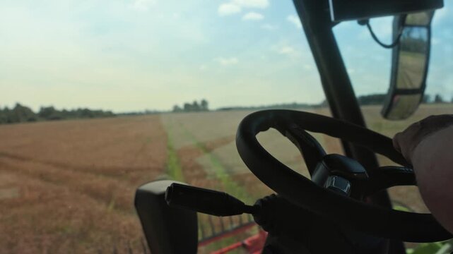 Operator steering a tractor through a wheat field during harvesting, showcasing the continuous action of threshing and harvesting in a rural agricultural setting