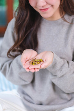 Vertical closeup image of a woman holding peeled pistachio nut in hands