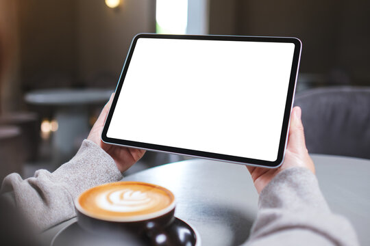 Mockup image of a woman holding digital tablet with blank white desktop screen in cafe