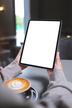 Vertical mockup image of a woman holding digital tablet with blank white desktop screen in cafe