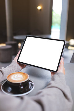 Vertical mockup image of a woman holding digital tablet with blank white desktop screen in cafe