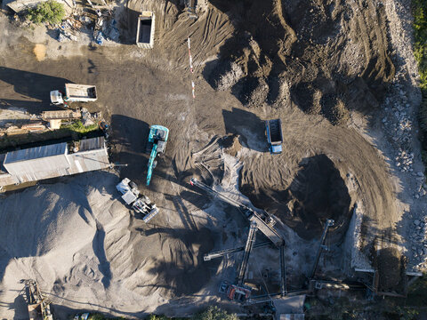 Aerial view of a stone crushing facility with heavy machinery, excavators, and trucks operating on a dusty site, surrounded by gravel piles in Kecamatan Karangnongko, Jawa Tengah, Indonesia.