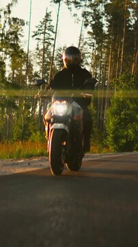 Motorcyclist riding along rural asphalt road at golden hour with sunlight reflecting on helmet visor and front wheel close-up capturing speed and freedom