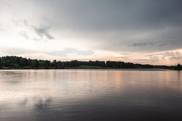 Fototapeta premium Tranquil view of a calm lake with reflections of cloudy skies and lush trees along the shoreline in a serene natural environment