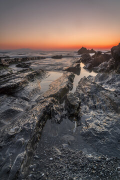 Vibrant sunset over the rocky coast of Barrika beach with long exposure sea water flowing between flysch rocks and golden glowing sun