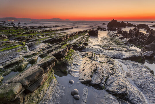 Vibrant sunset over the rocky coast of Barrika beach with long exposure sea water flowing between flysch rocks and golden glowing sun