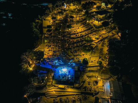 Aerial view of Puncak Sosok at night with an illuminated stage, terraced seating areas filled with people, and warm lighting in Kecamatan Pleret, Daerah Istimewa Yogya, Indonesia.