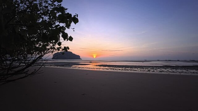 Sunset over tropical white sand beach with tidal flats and silhouetted island