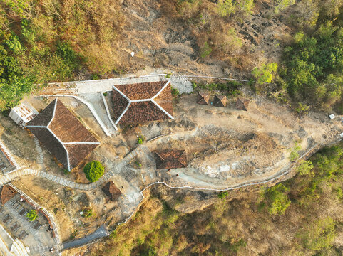Aerial view of Puncak Sosok with traditional Javanese-style buildings, dark tiled roofs, winding stone paths, and dry hilly terrain in Kecamatan Pleret, Daerah Istimewa Yogya, Indonesia.