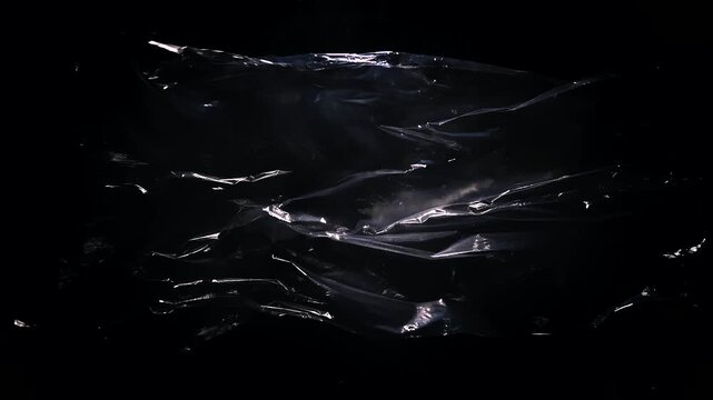 A transparent polyethylene sheet billows in wind, forming glossy folds on a black background. Concept packaging, material texture, abstract design and advertising.