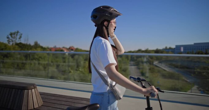 A young beautiful girl in casual clothes rides a bicycle on a bridge in the city in the morning during blue hour