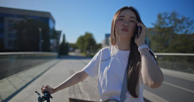 A young beautiful girl in casual clothes rides a bicycle on a bridge in the city in the morning during blue hour