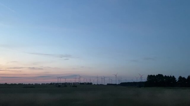 Mitfahrt auf der Autobahn bei Abendd&auml;mmerung mit Windr&auml;dern am Horizont. Roadtrip, Windenergie, Energiewende, Landschaft, Mobilit&auml;t und vorbeiziehende Infrastruktur am Stra&szlig;enrand.