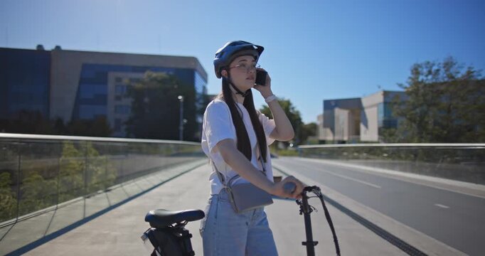 A young beautiful girl in casual clothes rides a bicycle on a bridge in the city in the morning during blue hour