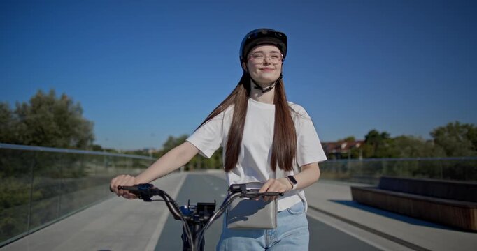 A young beautiful girl in casual clothes rides a bicycle on a bridge in the city in the morning during blue hour