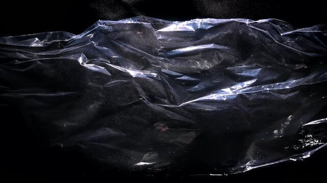A transparent polyethylene sheet billows in wind, forming glossy folds on a black background. Concept packaging, material texture, abstract design and advertising.