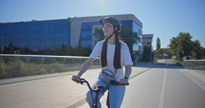 A young beautiful girl in casual clothes rides a bicycle on a bridge in the city in the morning during blue hour