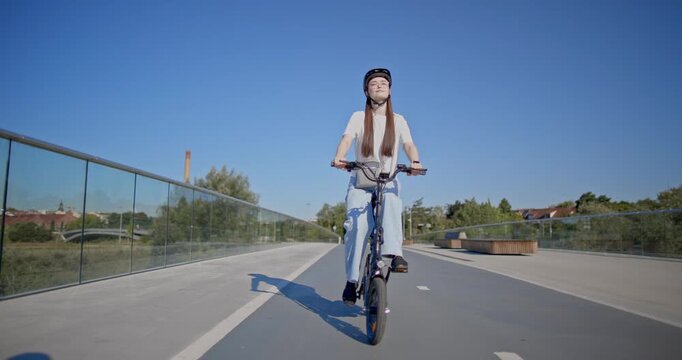 A young beautiful girl in casual clothes rides a bicycle on a bridge in the city in the morning during blue hour