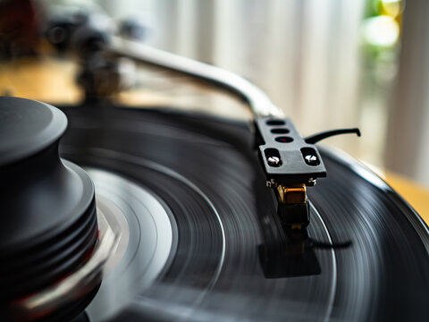 Close-up of spinning vinyl record on turntable, capturing motion of grooves and stylus. Classic analog music setup evokes nostalgia, creativity and warm sound
