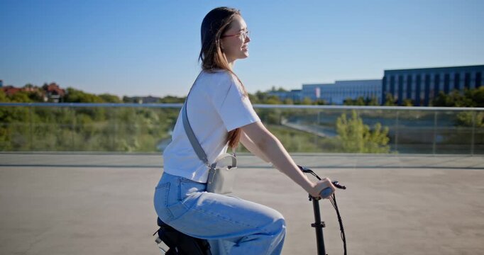 A young beautiful girl in casual clothes rides a bicycle on a bridge in the city in the morning during blue hour
