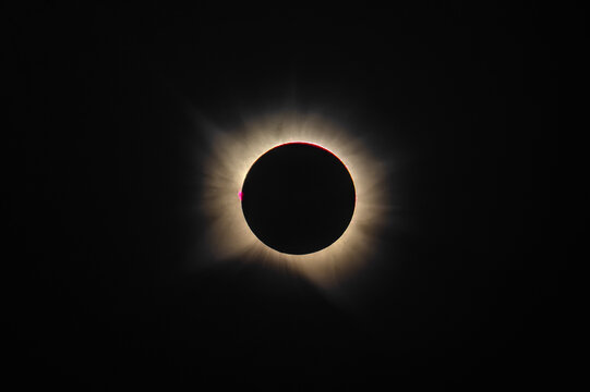Telephoto view of total solar eclipse totality showing bright solar corona and red prominences isolated on dark space background