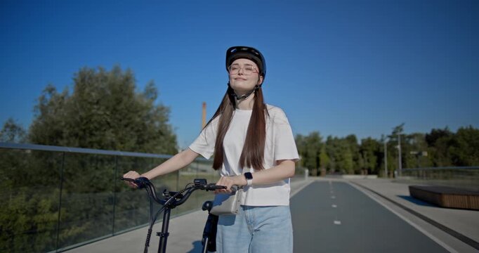 A young beautiful girl in casual clothes rides a bicycle on a bridge in the city in the morning during blue hour