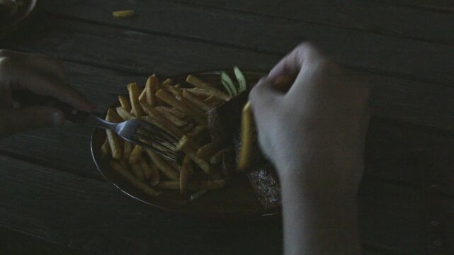 Close-up 4K video of a person using a fork to pick up a French fry from a plate of grilled meat and fries, then dipping it into red sauce during casual outdoor dining