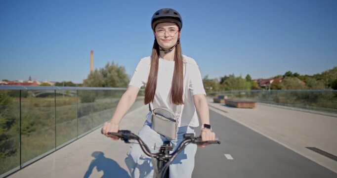 A young beautiful girl in casual clothes rides a bicycle on a bridge in the city in the morning during blue hour