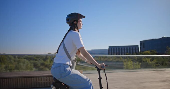 A young beautiful girl in casual clothes rides a bicycle on a bridge in the city in the morning during blue hour