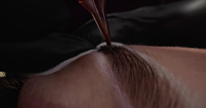 Slow motion probe closeup of micro blading pen depositing pigment into eyebrow skin in beauty studio..