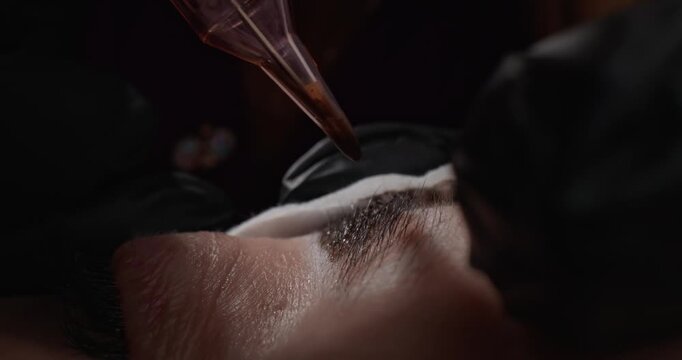 Handheld microblading artist applying permanent makeup pigment to eyebrow on client face in beauty studio.