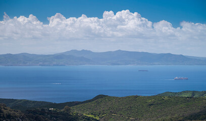 View across the Strait of Gibraltar from Cadiz, southern Spain, with the coast of Morocco visible in the distance. Calm blue sea, cargo ships and layered mountains under dramatic clouds. © ihervas