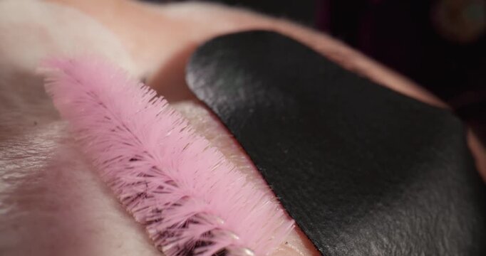 Handheld macro closeup of spoolie brushing and separating eyelashes over under eye pad in beauty studio with subtle tracking movement.